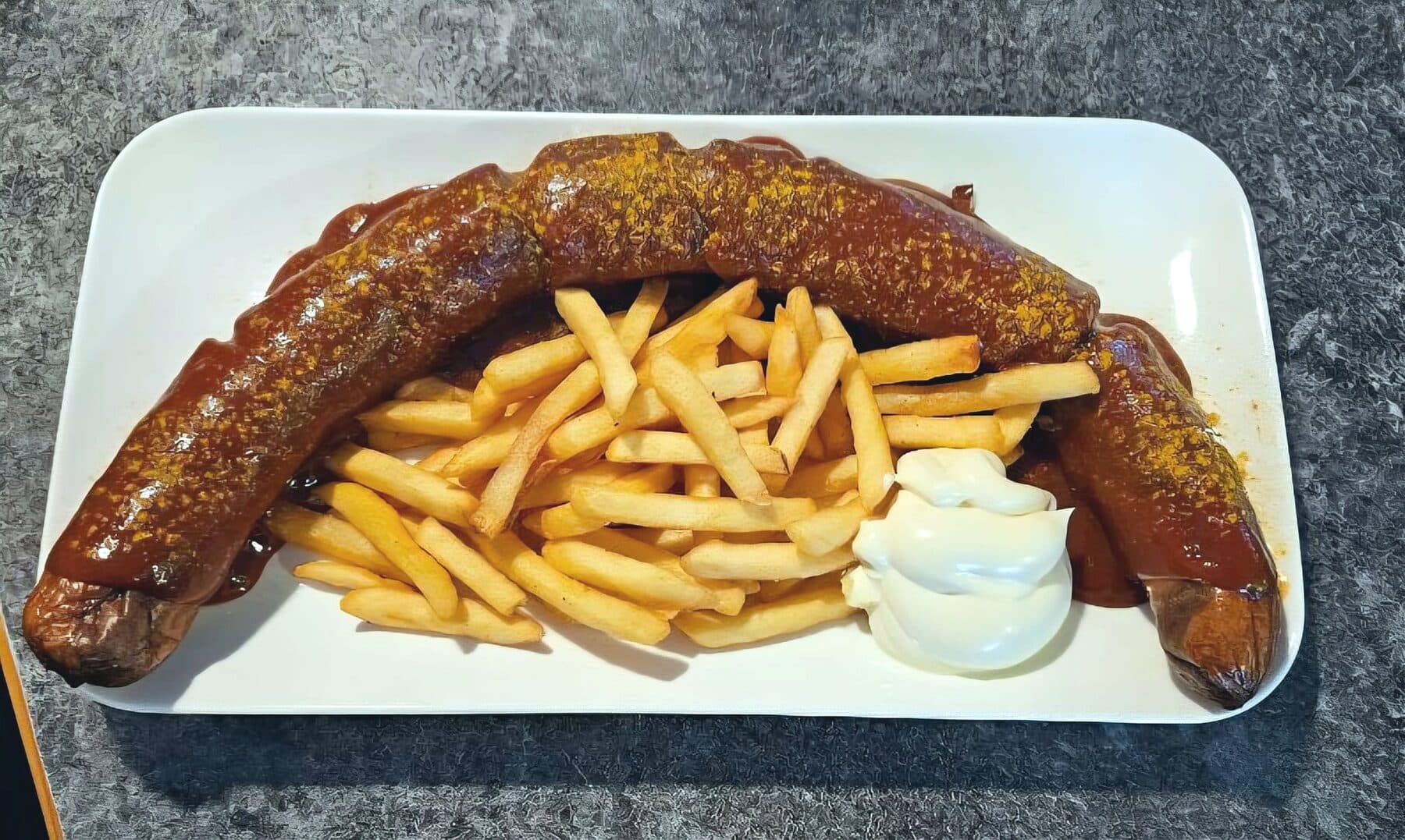 Currywurst mit Currysoße, Pommes und Mayonnaise auf einem weißen Teller